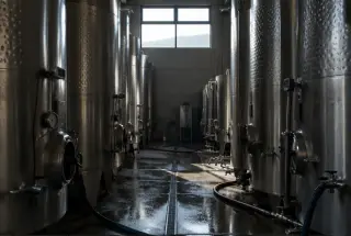 Cuves inox en contre-jour dans une cave de vinification, avec tuyaux et capteurs visibles.